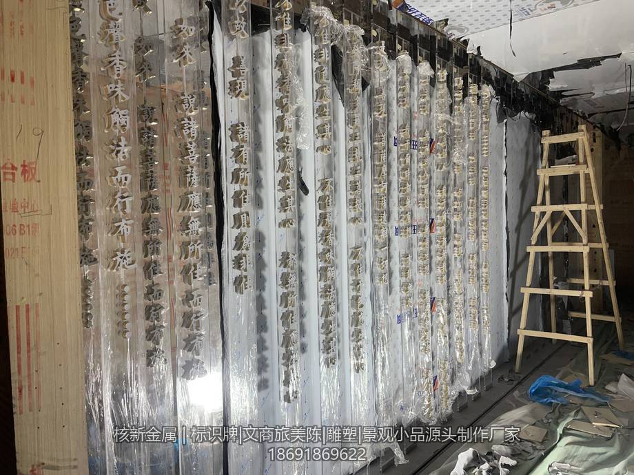 工厂车间内垂直排列的透明条板与金色书法字半成品,表面仍覆保护膜,旁边靠放木质人字梯,地面堆放包装材料